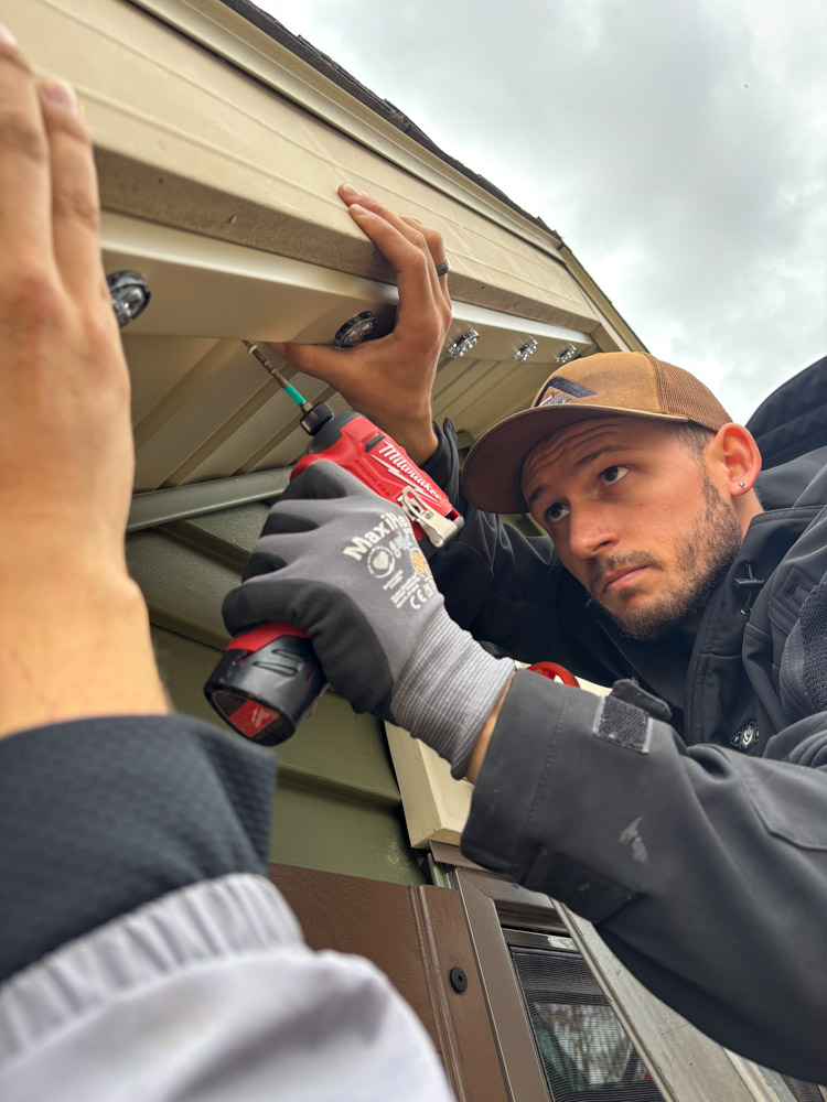 Meridian Outdoor Lighting technician installing permanent lighting under a soffit